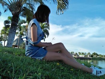 Woman sitting on grass against sky