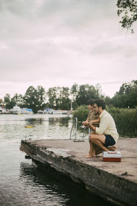 Side view of father and daughter fishing in lake during summer