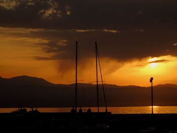 Silhouette sailboat on sea against orange sky