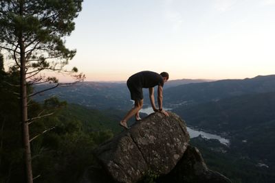 Man standing on rock looking at mountain against sky