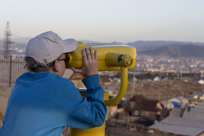 Boy is looking into big iron binocular on mountain viewpoint. travelling in beautiful places.
