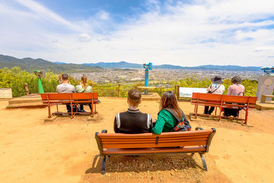 Rear view of people sitting on bench against the sky