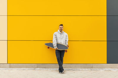 Full length portrait of young man standing against yellow wall