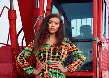 Portrait of young woman standing by red vehicle