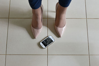 Low section of woman standing by damaged phone on tiled floor