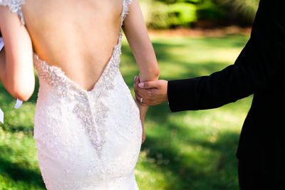 Rear view of wedding couple holding hands while walking on field