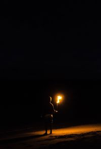Silhouette man standing on illuminated street against sky at night