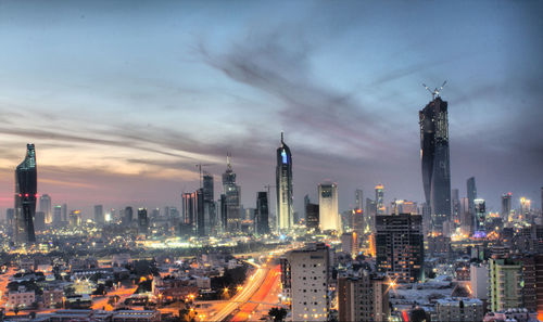 Illuminated buildings in city against cloudy sky