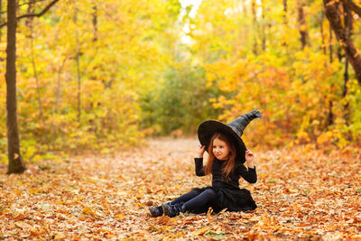 Portrait of young woman sitting on leaves during autumn