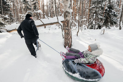 Joyful dad rides his daughter on a sleigh in the snowy forest