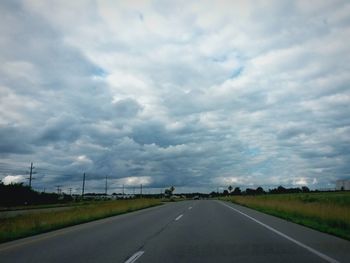 Empty road passing through field against cloudy sky