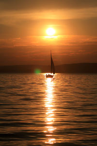 Silhouette sailboat in sea against sky during sunset