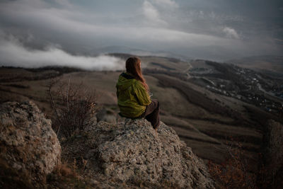 Rear view of woman sitting on rock against landscape