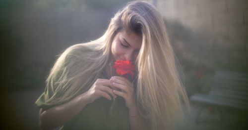 Woman with eyes closed smelling red flower