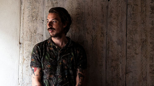 Portrait of young man looking away while standing against wall
