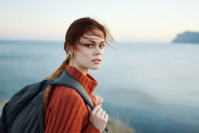 Portrait of young woman looking at sea against sky