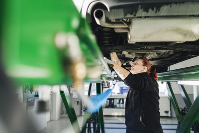 Side view of female mechanic repairing car on hydraulic lift