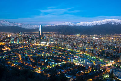 Aerial view of illuminated cityscape against snowcapped mountains during sunset