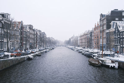 Sailboats moored on canal amidst buildings in city against clear sky