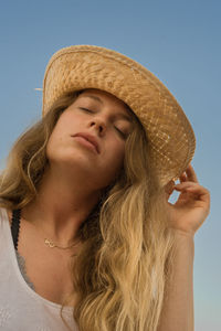 Low angle view of young woman wearing hat against clear sky