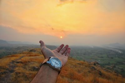 Cropped hand of man reaching sky during sunset