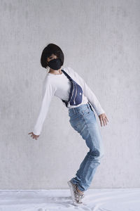 Full length of woman wearing mask dancing against wall