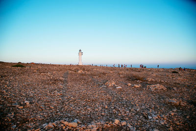 Lighthouse on beach against clear blue sky