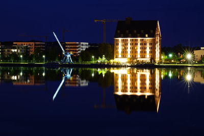 Reflection of illuminated buildings in lake against sky at night