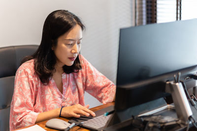 Businesswoman working on laptop sitting at her office desk with desktop computer.