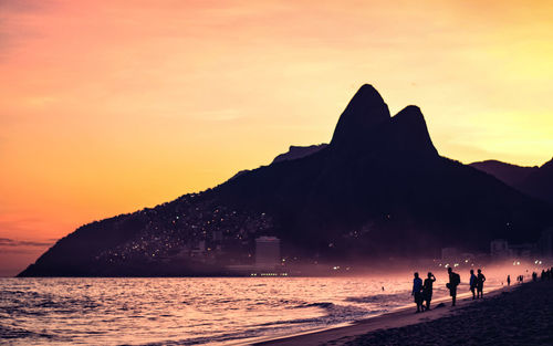 Silhouette people on beach against orange sky