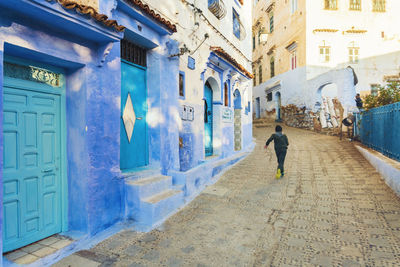 Rear view of man walking on street amidst buildings