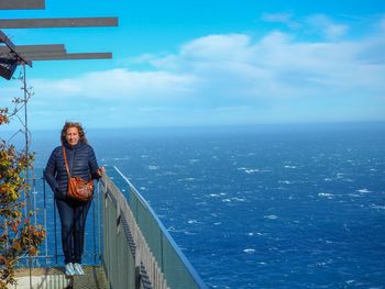 Woman standing by railing against sea