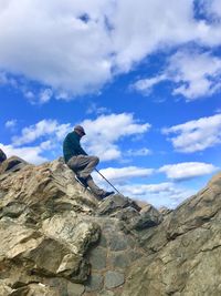 Low angle view of man sitting on rocky mountains against sky