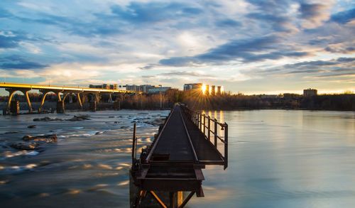 Jetty over river against cloudy sky during sunset