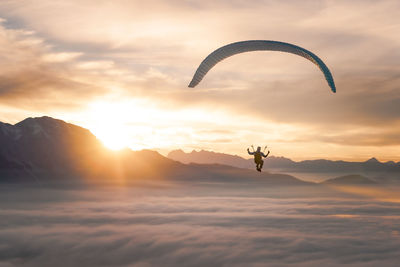 Man paragliding over clouds against cloudy sky during sunset