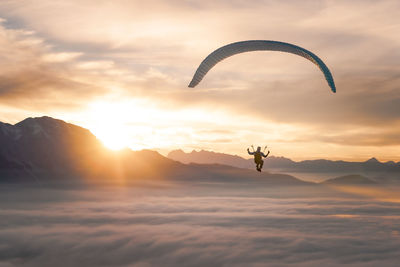 Silhouette person paragliding against sky during sunset