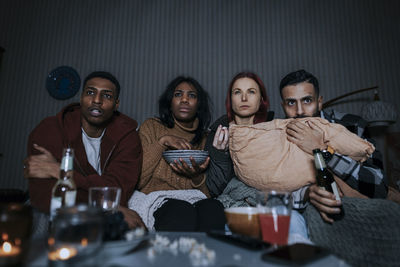 Multiracial friends wih food and beer watching scary movie together in cabin