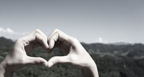 Close-up of hand holding heart shape against sky