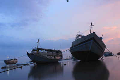 Sailboats moored on sea against sky during sunset