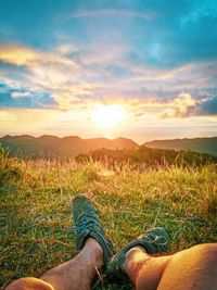 Low section of person on field against sky during sunset