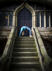 Young woman in bridge position practicing yoga on staircase against church