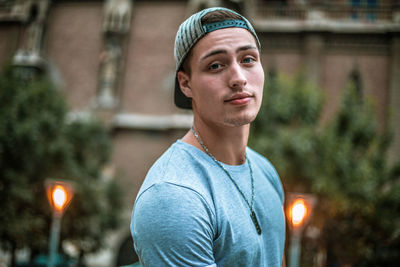 Close-up portrait of young man wearing cap while standing against building