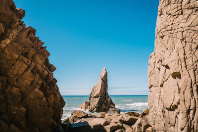 Rock formations at beach against blue sky