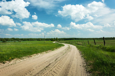 Dirt road amidst field against sky