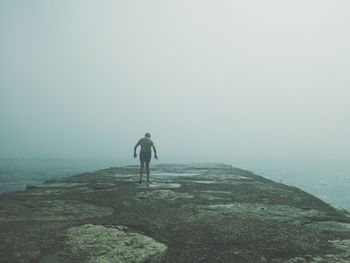 Rear view of man walking on beach during foggy weather