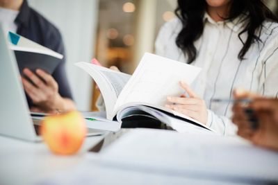 Midsection of friends studying with books at table in university