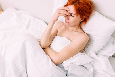 Portrait of a young sad tired woman lying in bed. illness and headache