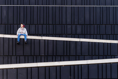 Young teen sitting on a fence while using headphones to listen music