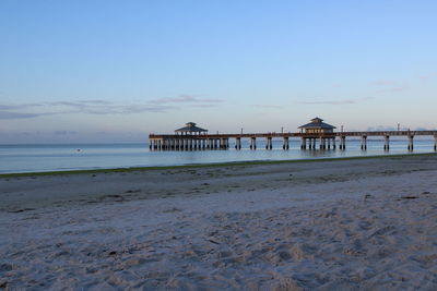 Pier on beach against sky during sunset