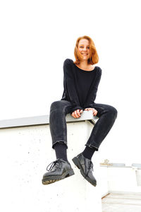 Portrait of smiling young woman sitting against wall